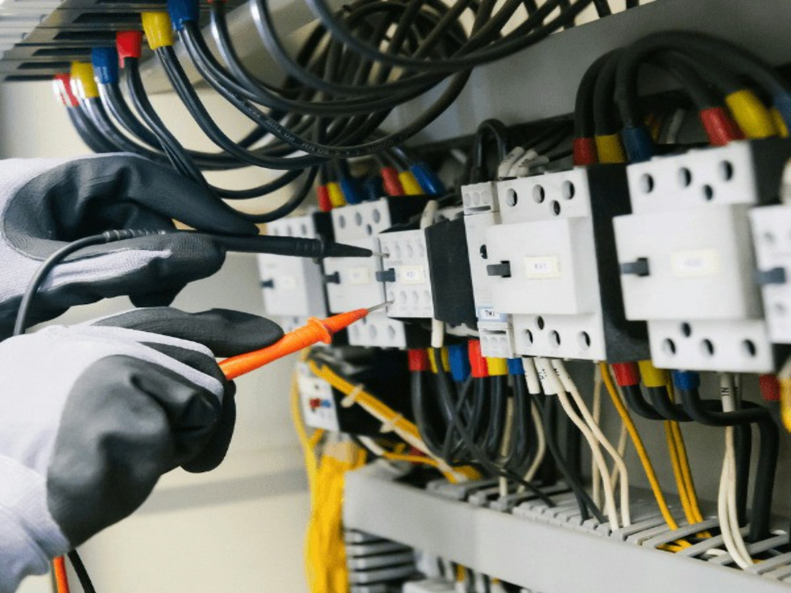 Electrician testing a commercial electrical panel with a multimeter during a maintenance inspection