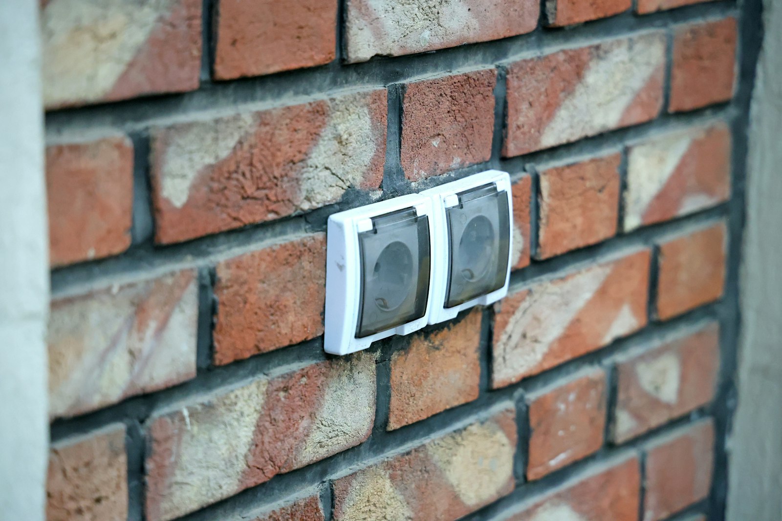 Two outdoor electrical outlets with weatherproof covers mounted on an exterior brick wall